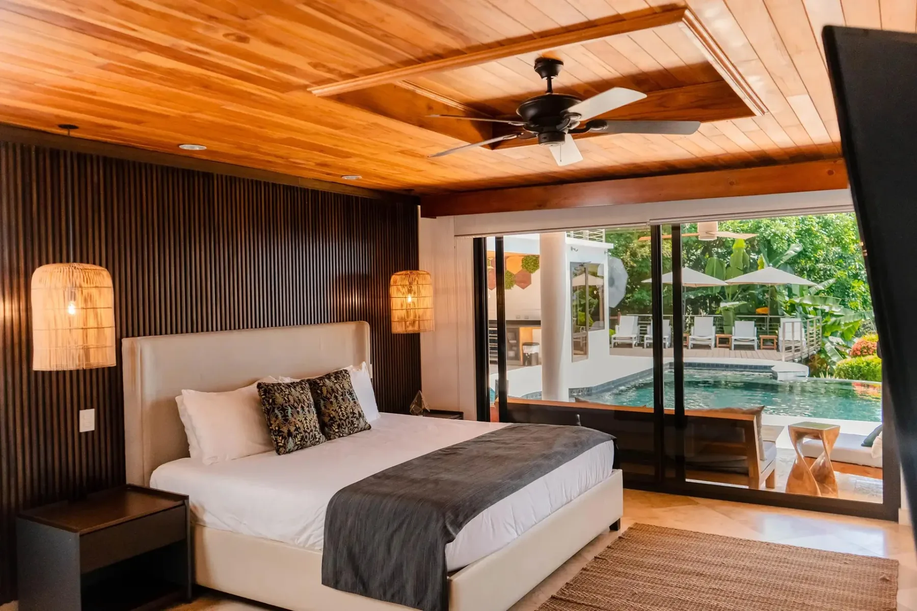 A bedroom with a bed and sliding glass doors opening onto a pool and garden.