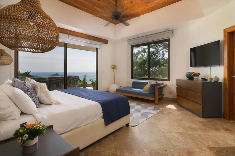 Casa Anjali Luxury Villa · 27. This king bedroom features a vaulted teak ceiling and is filled with natural light from glass doors opening to an ocean-view terrace and a window overlooking the rainforest.