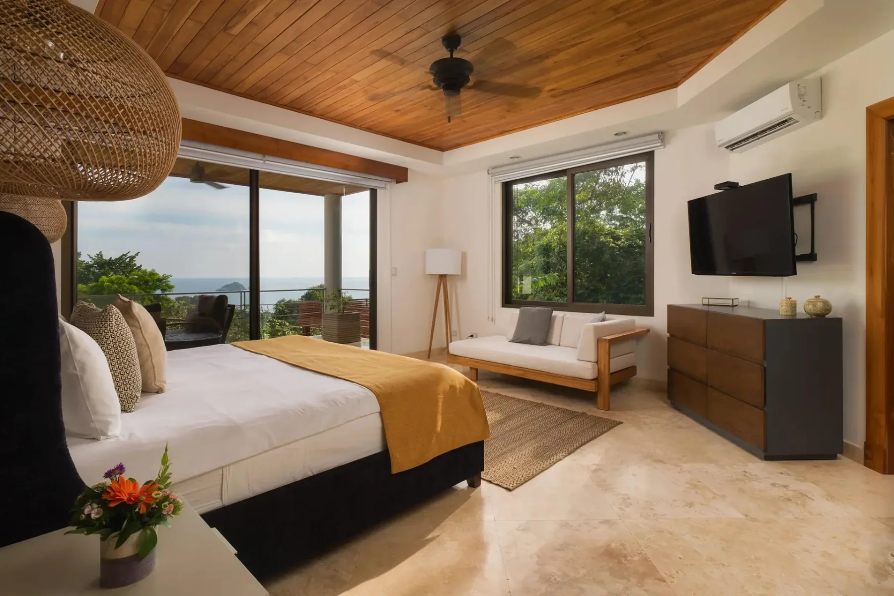 A bedroom with a bed, a seating area, and glass doors opening onto a balcony.
