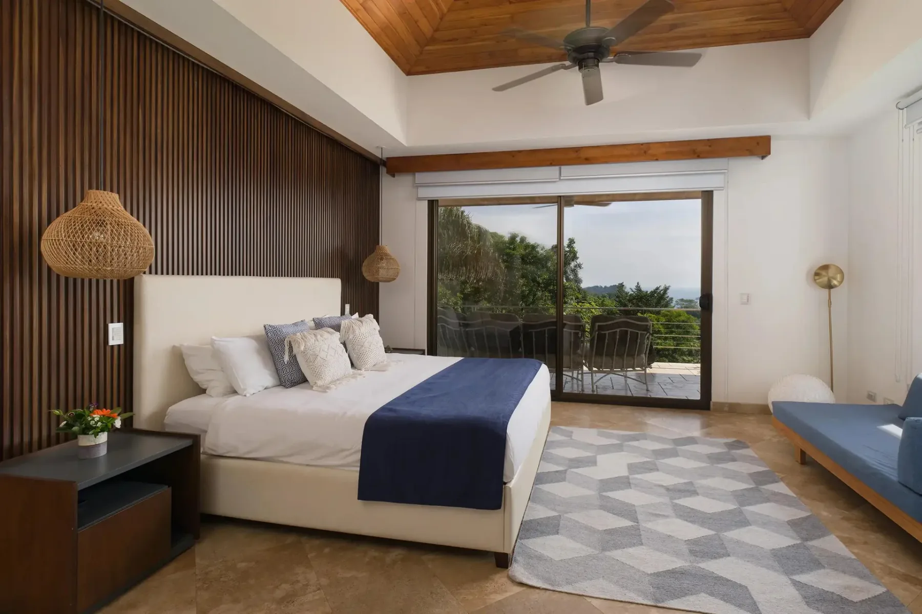 A bedroom with a large bed, geometric rug, and sliding glass doors opening to a balcony.