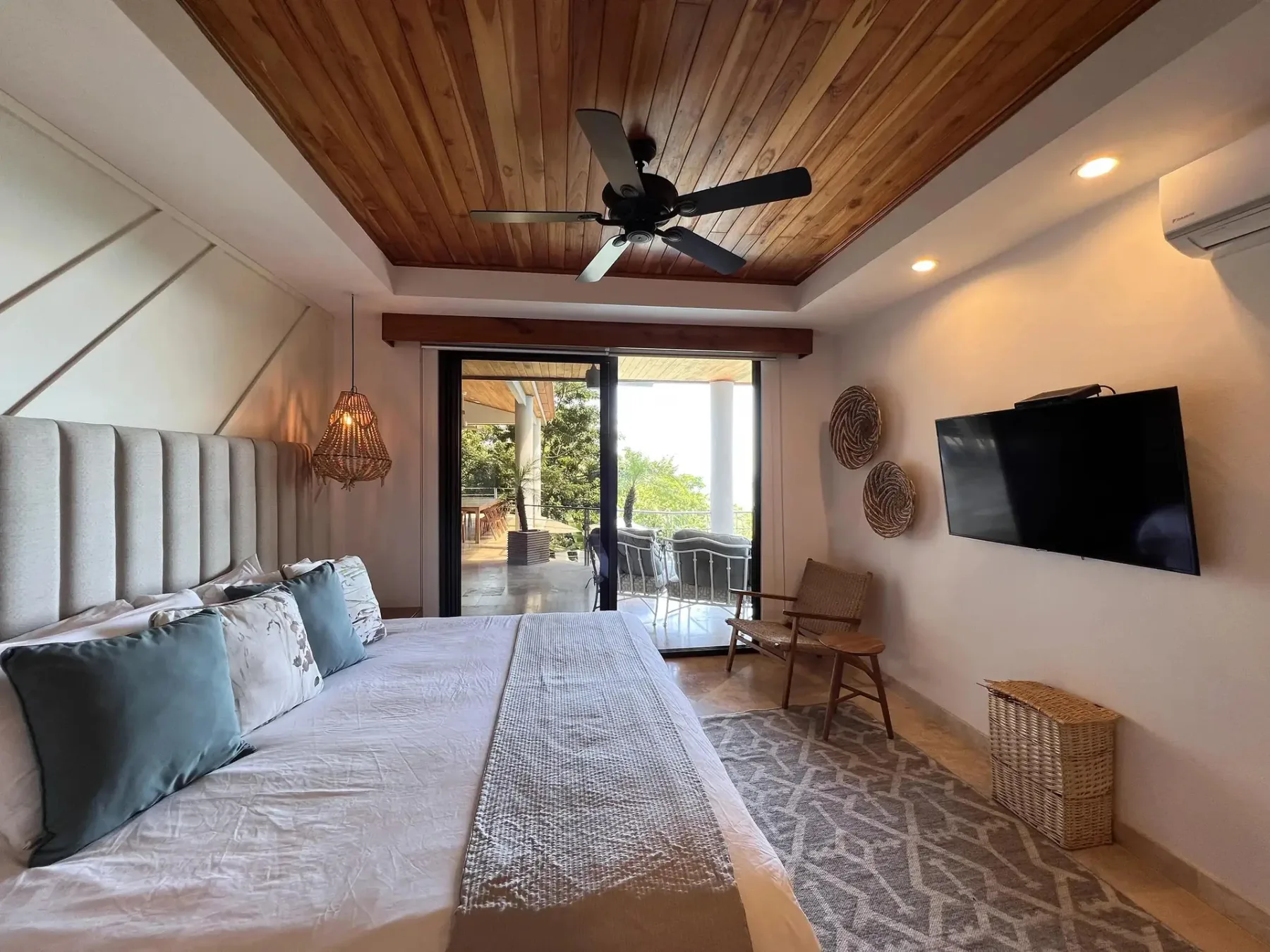 A bedroom with a large bed, a wall-mounted television, and glass doors opening onto a balcony.