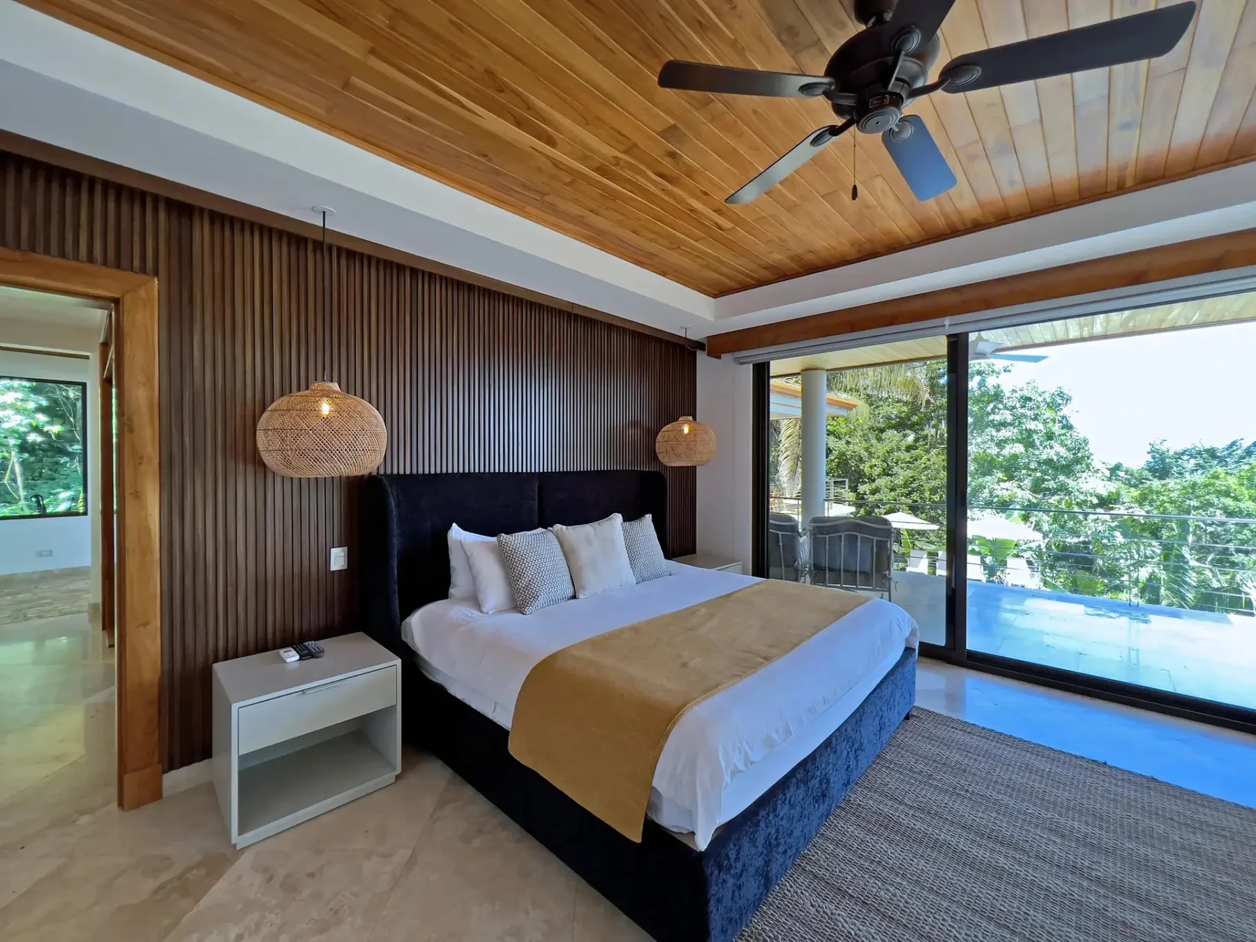 A bedroom with a bed, wood-paneled ceiling, and sliding glass doors opening onto a terrace.
