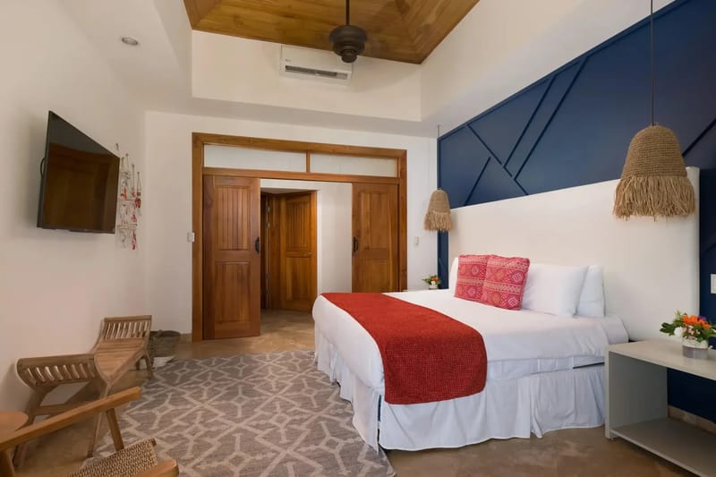 Casa Anjali Luxury Villa · 33. This bedroom features a king bed with a white headboard, a navy blue geometric accent wall, a vaulted teak ceiling, and wooden sliding doors leading to an adjoining space.