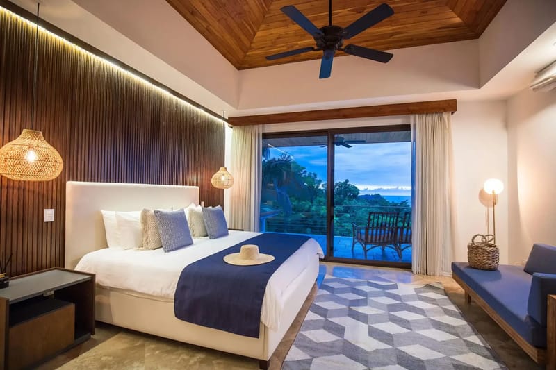 Casa Anjali Luxury Villa · 21. A king bedroom with a vaulted teak ceiling and a slatted accent wall opens through floor-to-ceiling glass doors to a private terrace with rainforest and ocean views.
