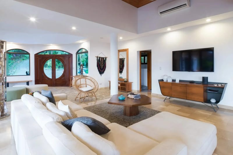 Casa Anjali Luxury Villa · 15. The spacious living room offers a vaulted teak ceiling and tiled floors, with large arched doors and windows bringing in natural light and views of the surrounding rainforest.