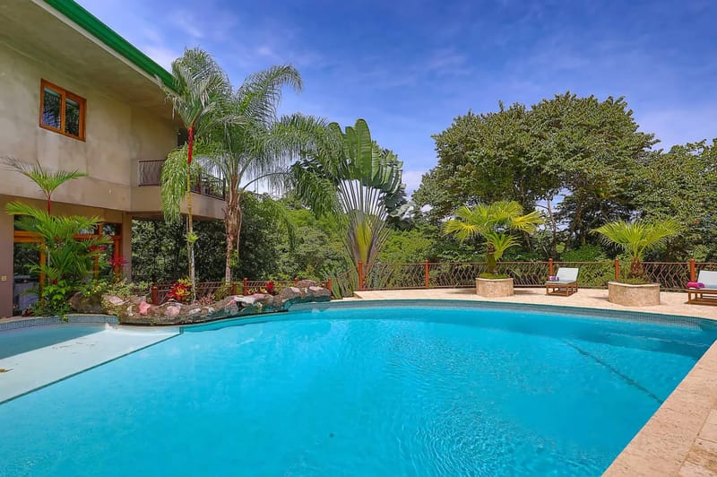Casa Estrella del Mar · 15. A bright blue outdoor swimming pool is set against a multi-level villa with wood-framed windows and surrounded by lush tropical rainforest under a sunny sky.