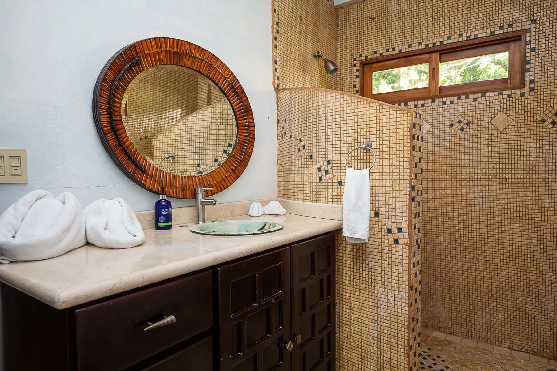 A bathroom with a dark vanity, round mirror, and tiled shower.