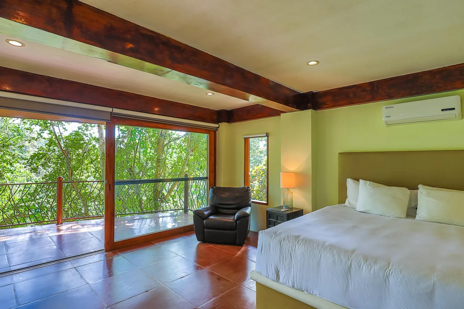 A bedroom with a bed and wide glass doors opening onto leafy greenery.