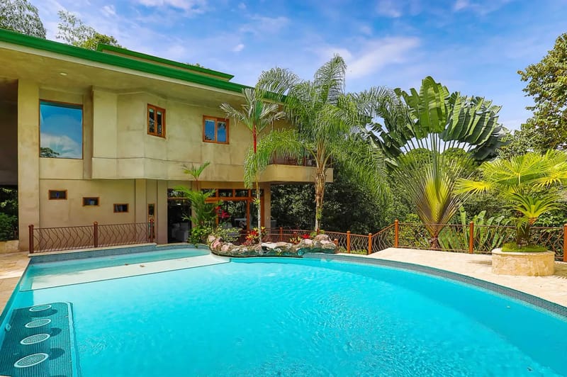 Casa Estrella del Mar · 17. The multi-level villa's facade overlooks an extensive outdoor swimming pool and sun deck, all enveloped by tropical rainforest under a bright sky.