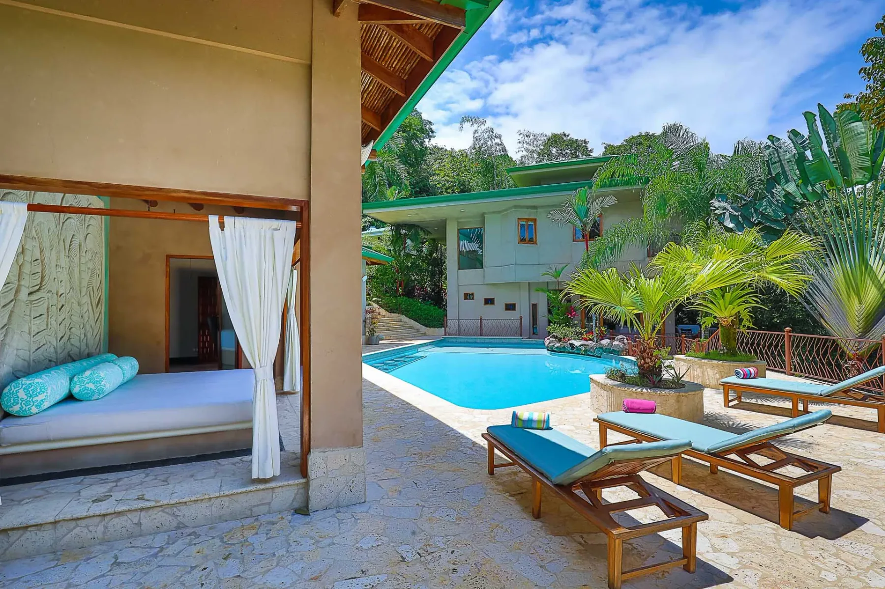 A bright courtyard features a swimming pool, outdoor seating, and a curtained daybed.