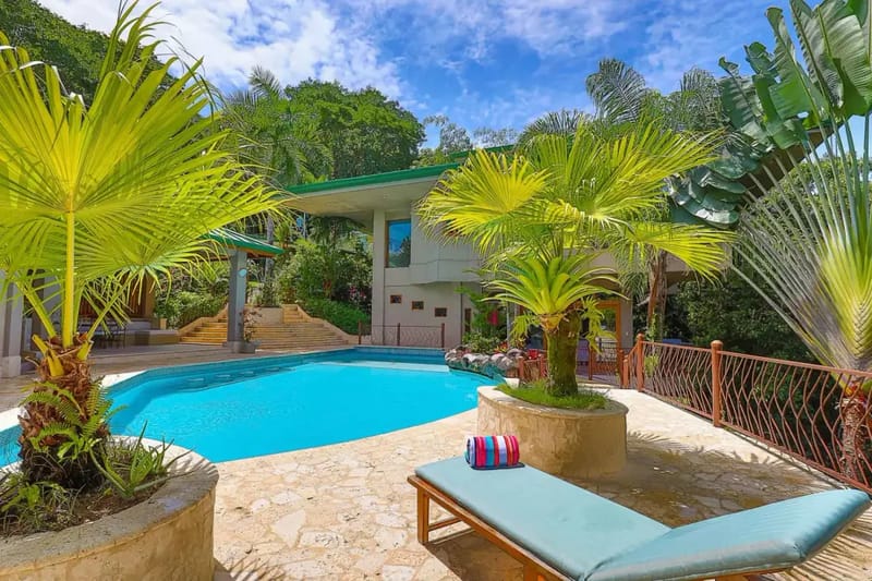 Casa Estrella del Mar · 14. The outdoor pool area features a large swimming pool, a stone patio, and tropical foliage, with a contemporary multi-level villa visible against a backdrop of dense rainforest.