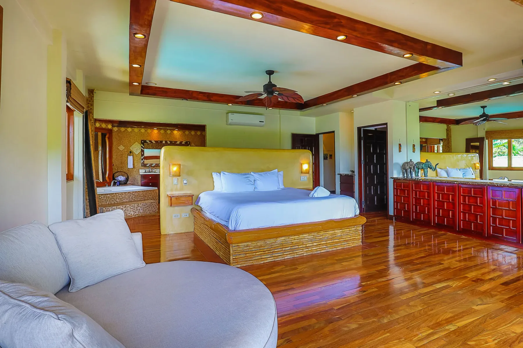 A spacious bedroom with a large bed, polished wood flooring, and a ceiling fan.