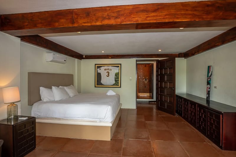 Casa Estrella del Mar · 39. This bedroom features a large bed under exposed wooden ceiling beams, terracotta-style flooring, and an open doorway leading to a private bathroom.