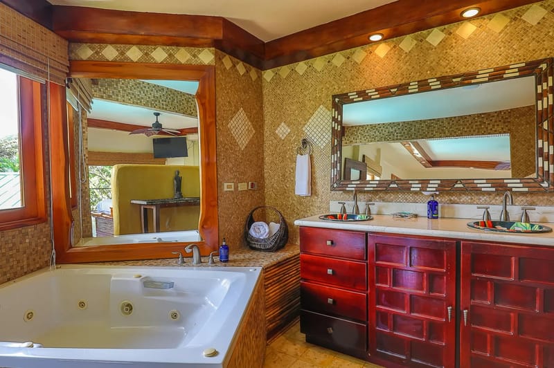 Casa Estrella del Mar · 32. A spacious bathroom features a jetted tub, a double vanity with dark wood cabinetry, and mosaic-tiled walls, with a large window providing natural light and views of tropical foliage.