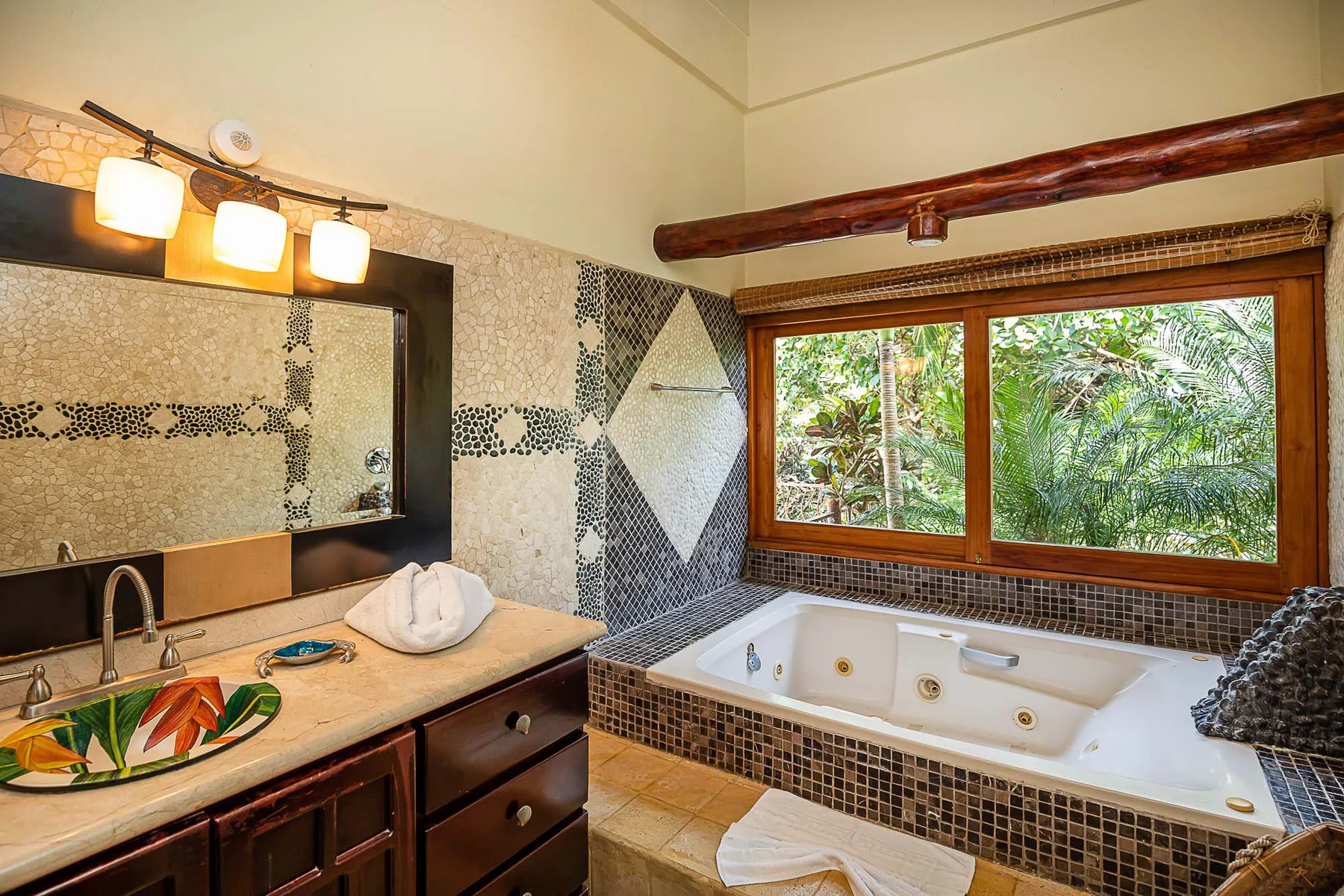 A bathroom with a bathtub beside a wide window overlooking green foliage.