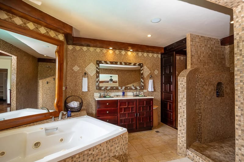 Casa Estrella del Mar · 33. A spacious bathroom designed with warm mosaic tiling and dark wood accents features a jetted tub, a walk-in shower, and a dual vanity with a patterned mirror.