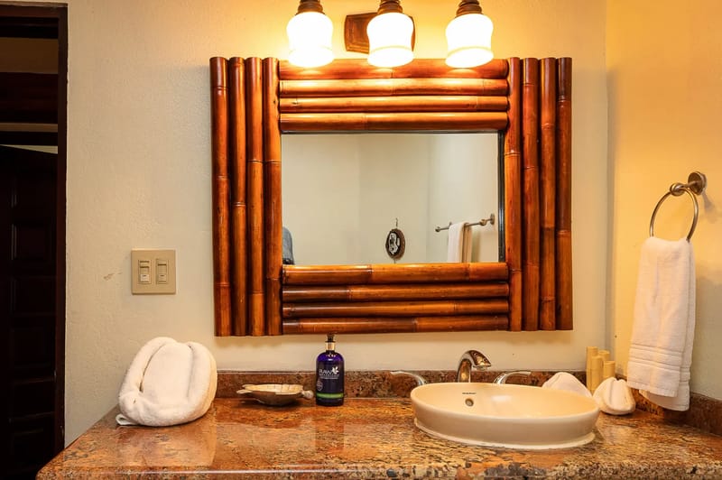 Casa Estrella del Mar · 44. This bathroom features a vessel sink set in a speckled stone countertop, beneath a mirror framed with natural bamboo and illuminated by warm wall sconces.