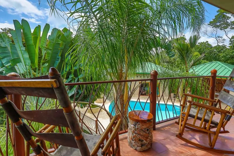 Casa Estrella del Mar · 31. An open-air terrace with a tiled floor and rustic wooden seating overlooks the inviting pool and surrounding tropical forest under natural light.
