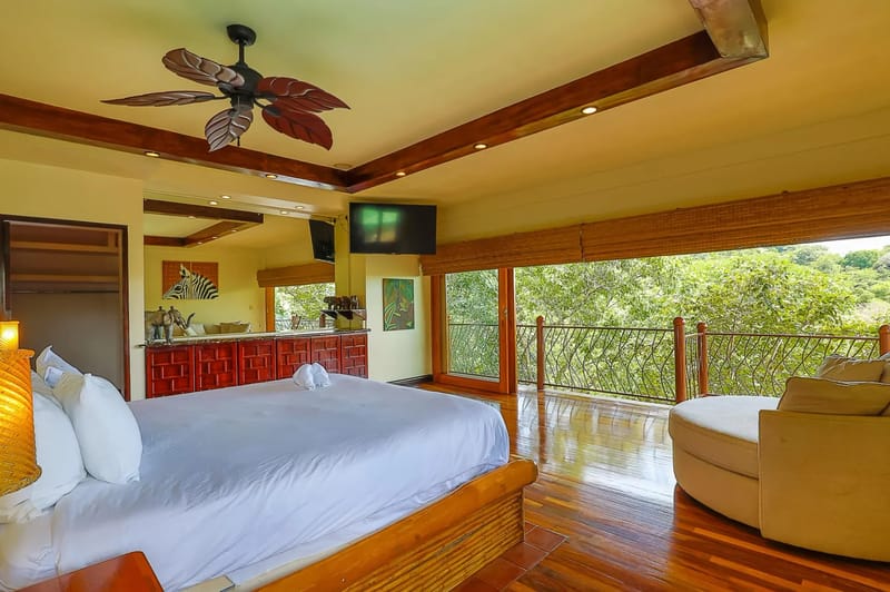 Casa Estrella del Mar · 38. This bedroom offers a large bed, polished wood floors, and floor-to-ceiling glass doors that open to a private balcony overlooking the rainforest, providing natural light and an open-air feel.