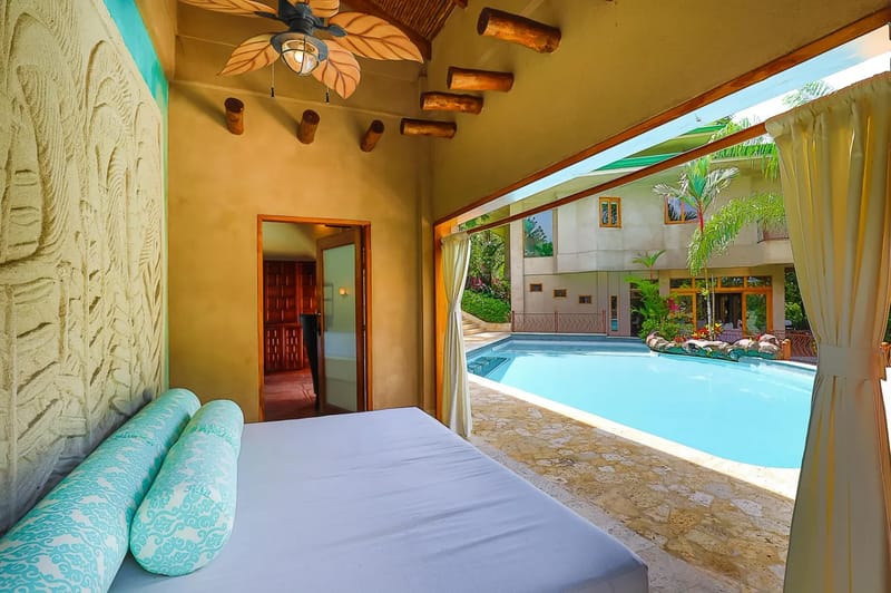 Casa Estrella del Mar · 12. This covered outdoor lounge features a daybed, exposed wooden beams, and a leaf-bladed ceiling fan, with open views to the pool and the main villa.
