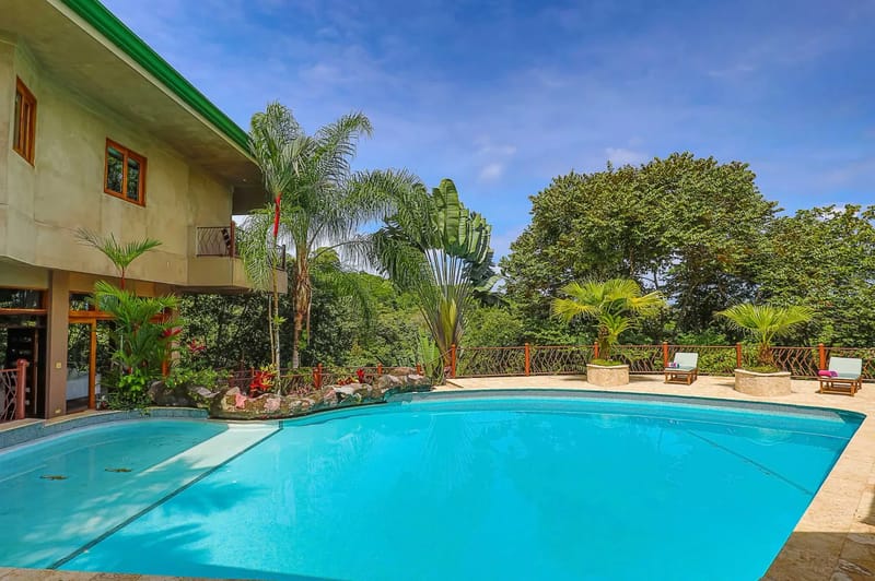 Casa Estrella del Mar · 18. A large blue swimming pool is set against a multi-story villa, surrounded by tropical forest greenery under a bright blue sky.