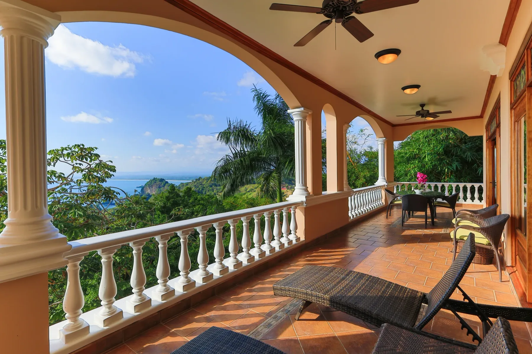 A covered terrace with outdoor seating overlooks a green landscape and the sea.