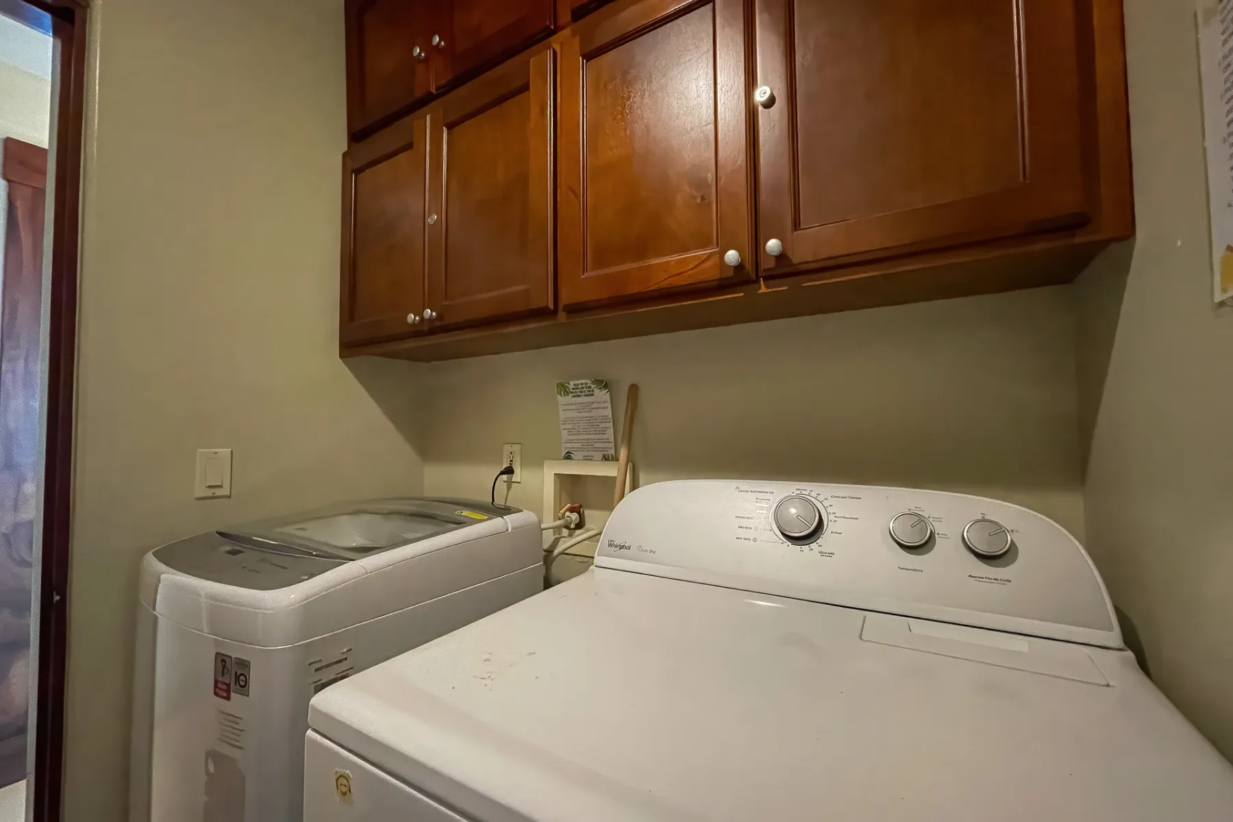 A laundry area with a washing machine and dryer beneath wooden cabinets.
