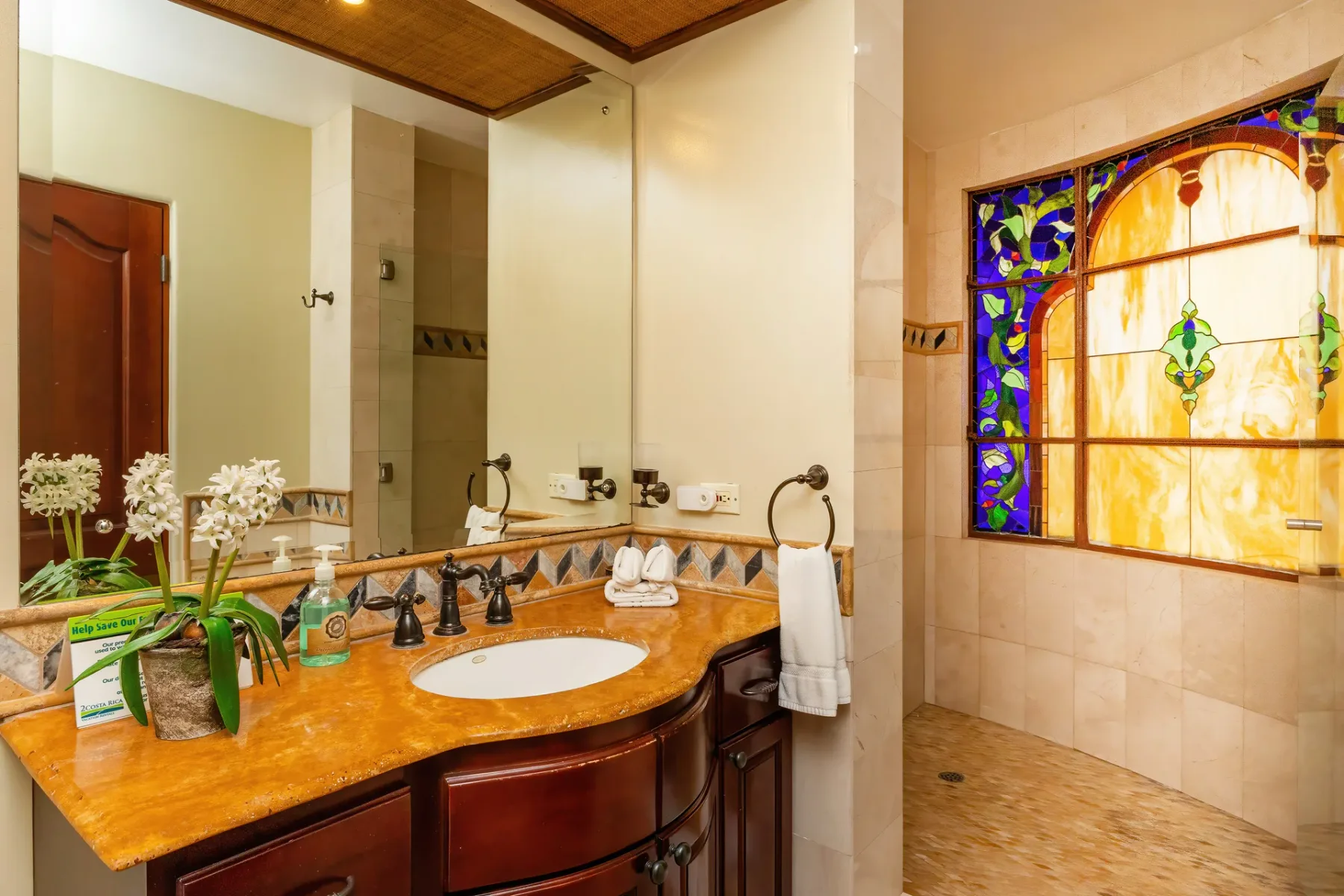 A bathroom vanity with a sink sits beside a colorful stained-glass window.