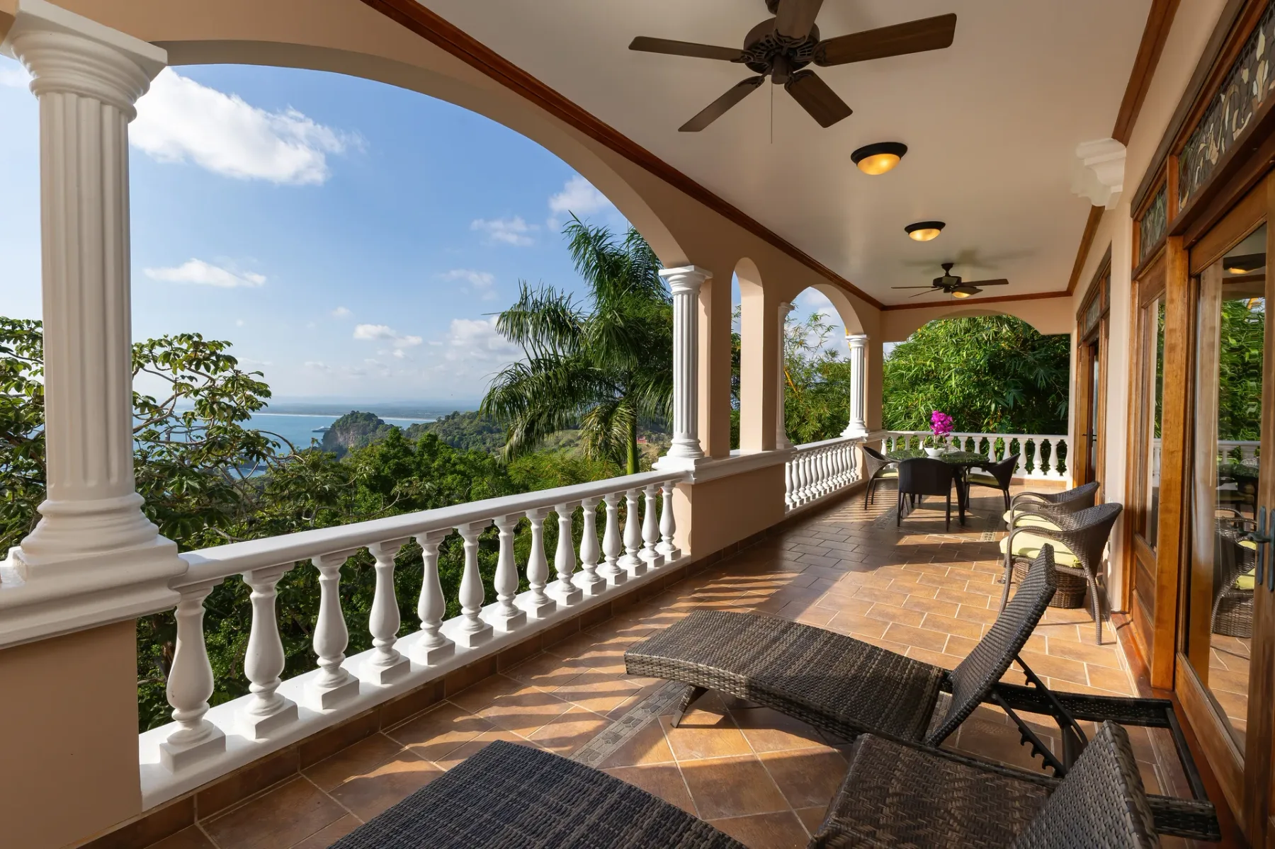 A covered terrace with seating overlooks lush greenery and the sea.