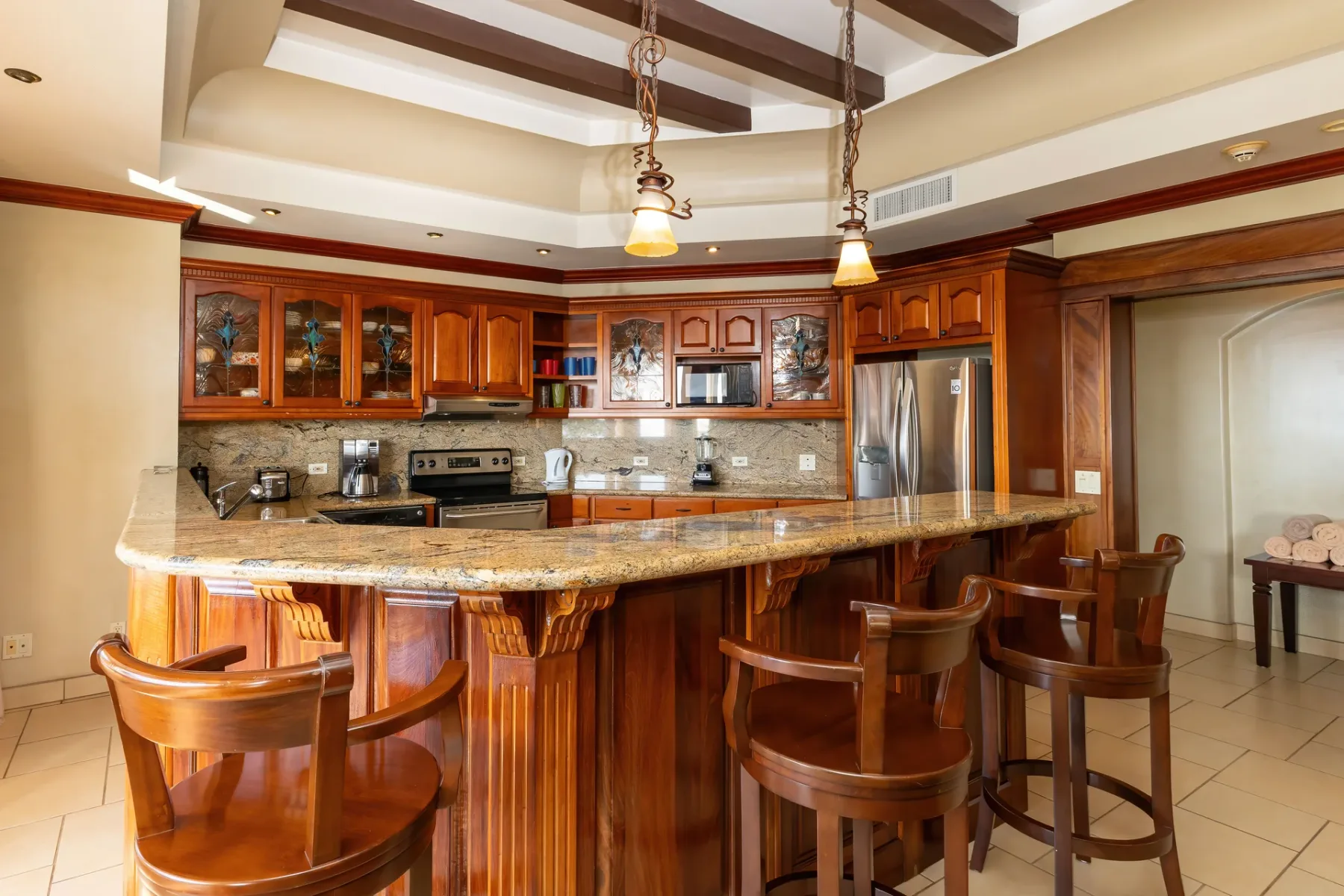 A kitchen with a large island and wooden seating beneath pendant lights.