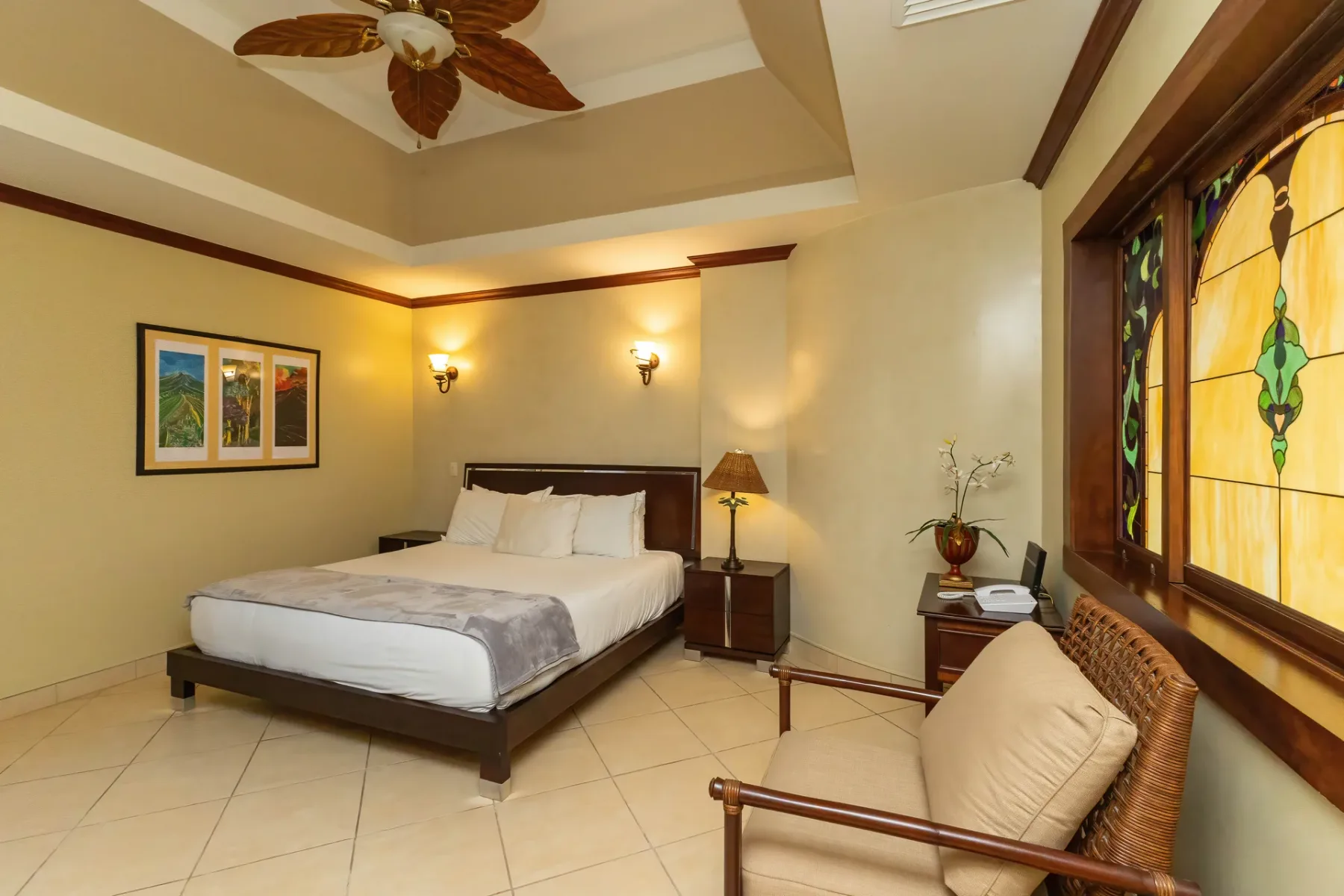 A bedroom with a bed and a seating area beside a stained-glass window.