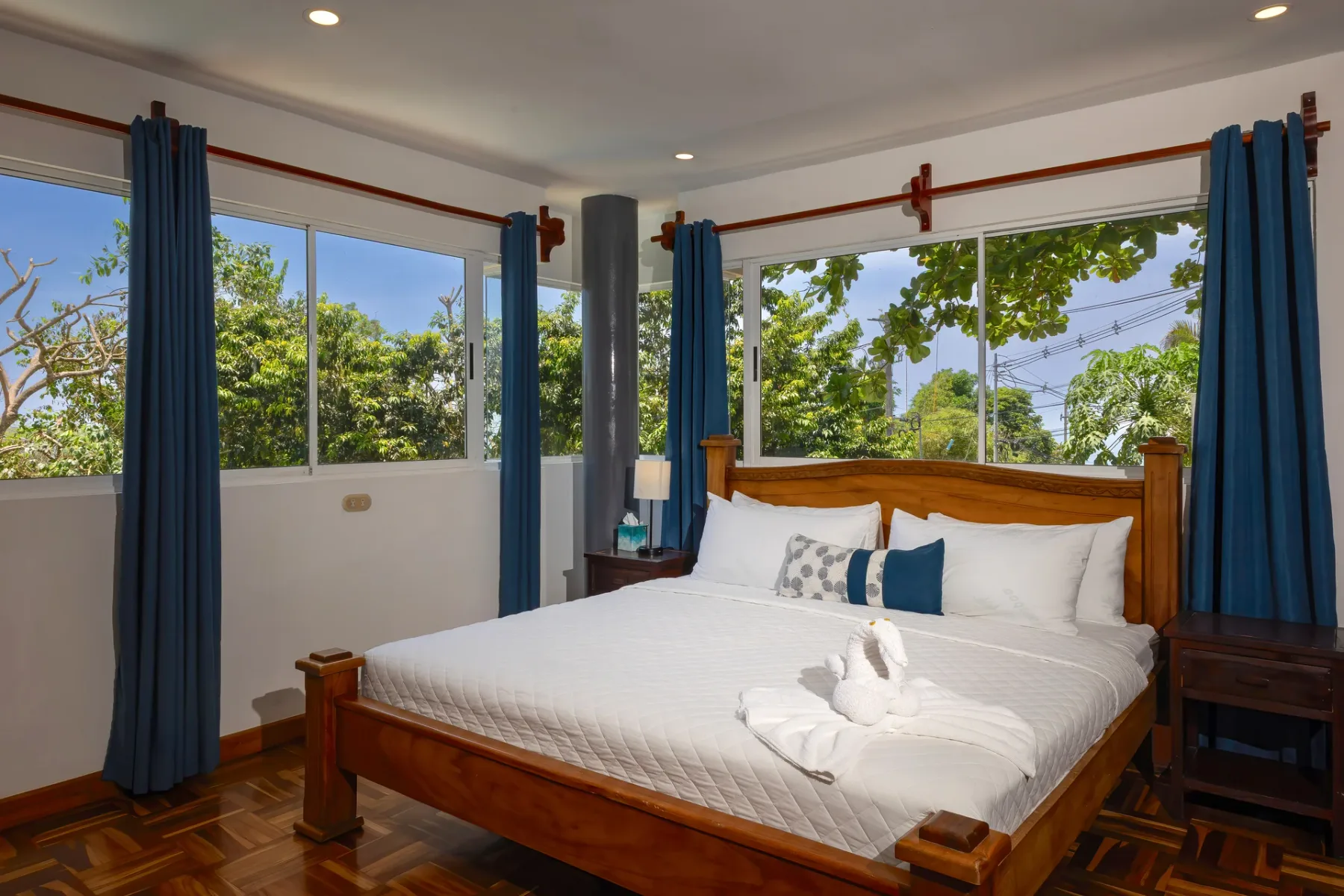 A bedroom with a wooden bed, white bedding, and large windows overlooking greenery.