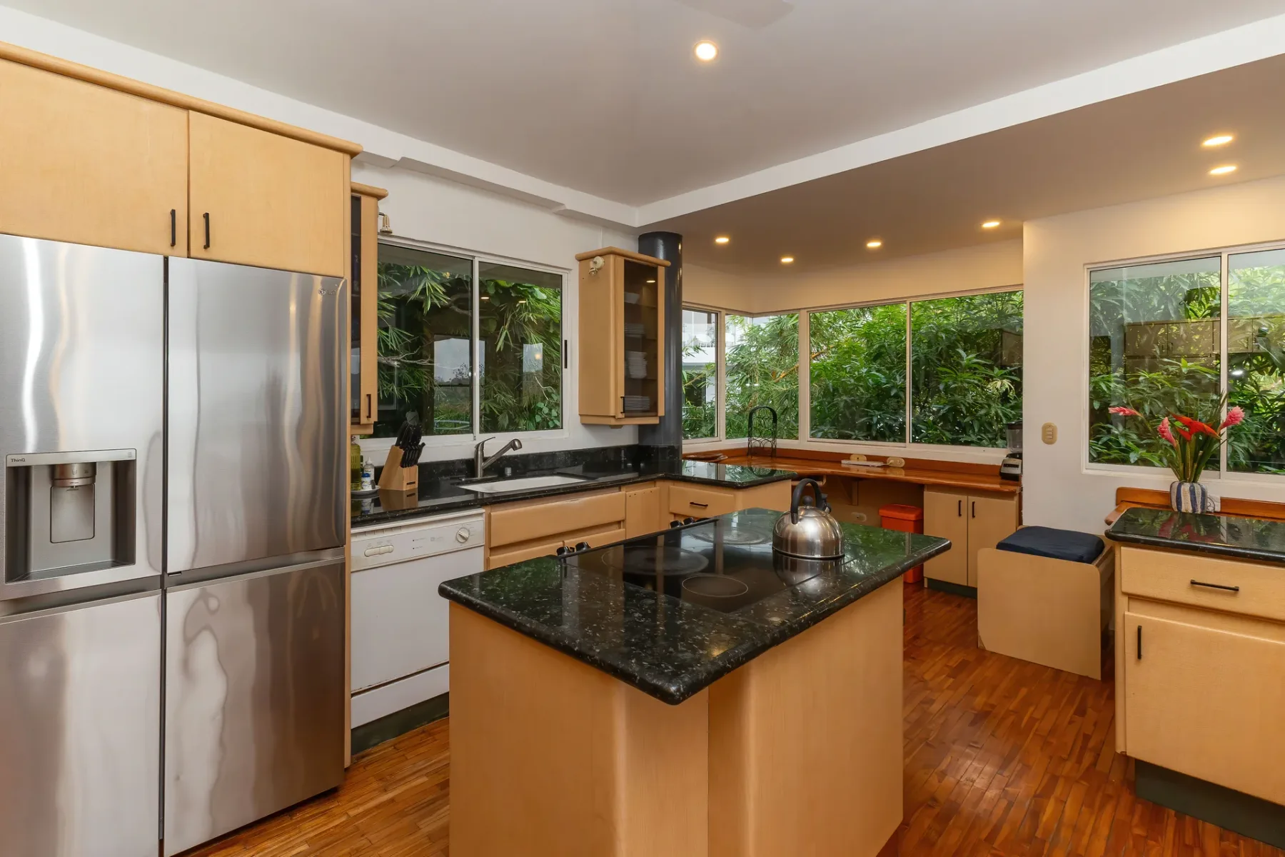 A spacious kitchen with wood cabinetry, a central island, and windows overlooking greenery.