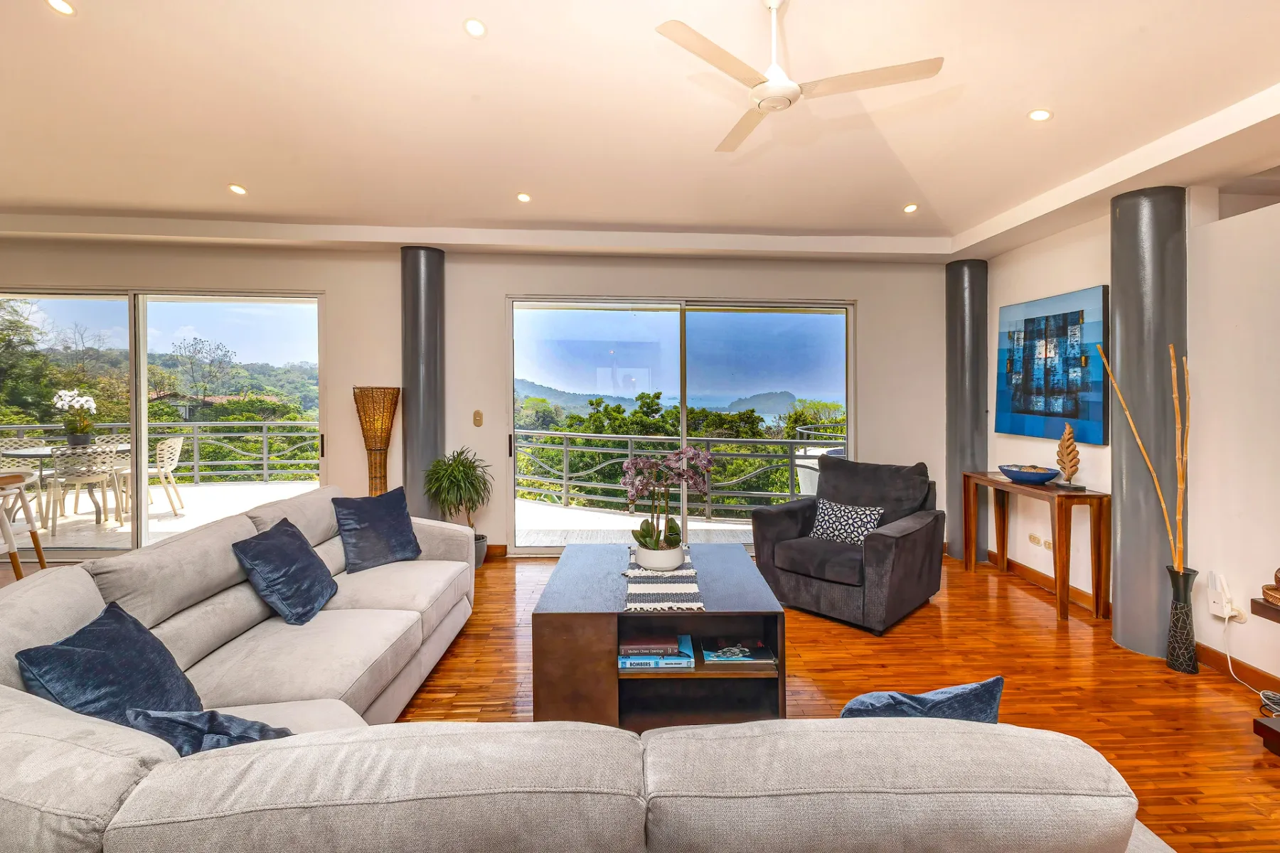 A bright living room has seating, a coffee table, and large windows overlooking greenery.