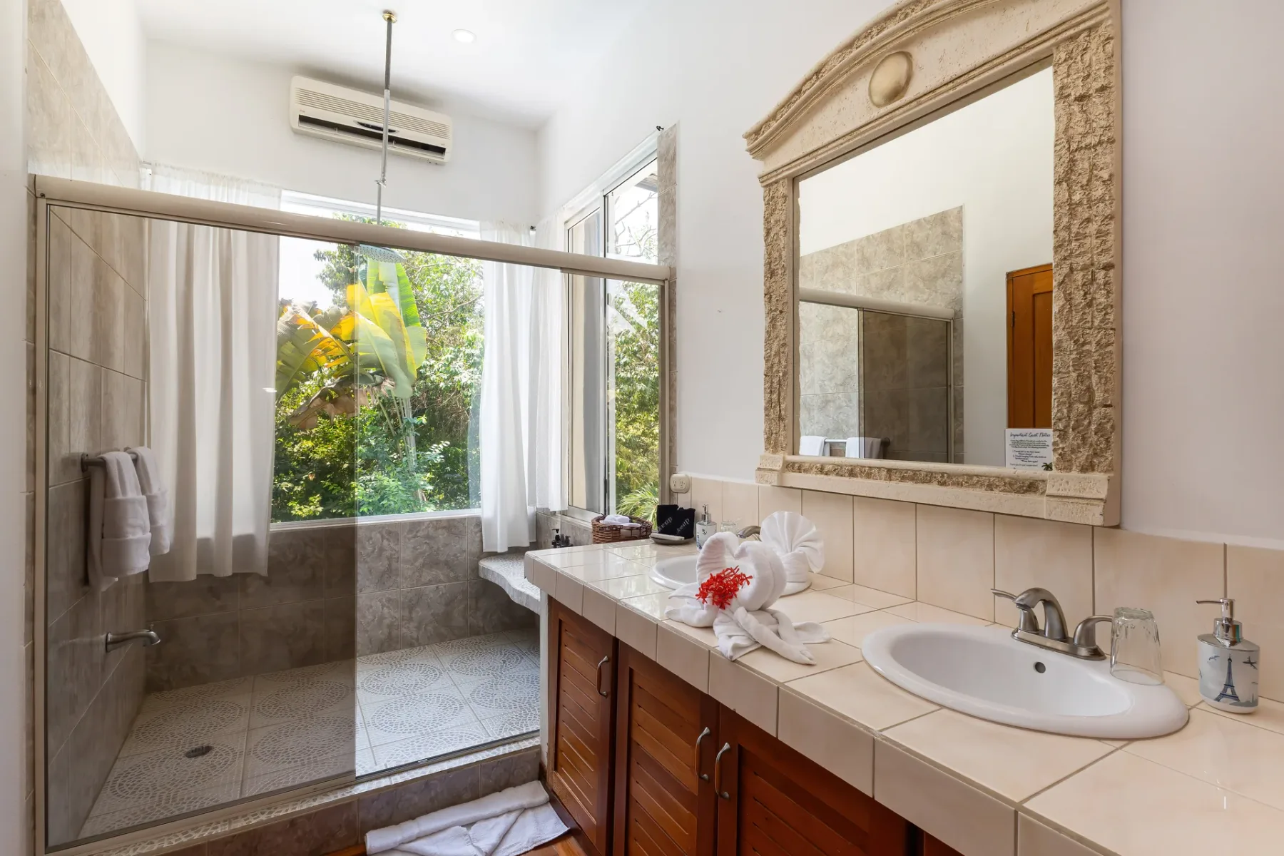 A bright bathroom with a sink, large mirror, and glass shower.
