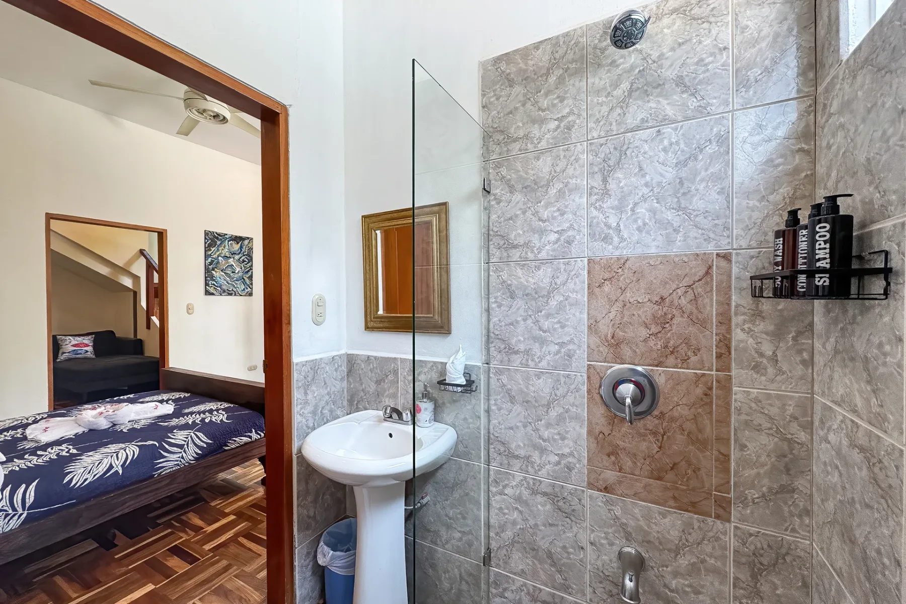 A tiled bathroom with a sink and shower beside a bedroom.
