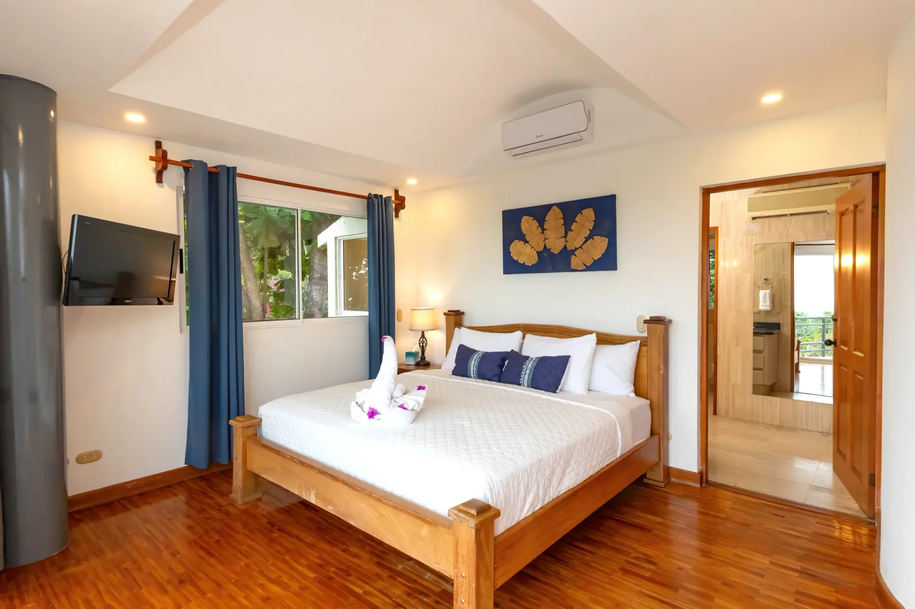 A bedroom with a wooden bed, blue curtains, and a wall-mounted television.
