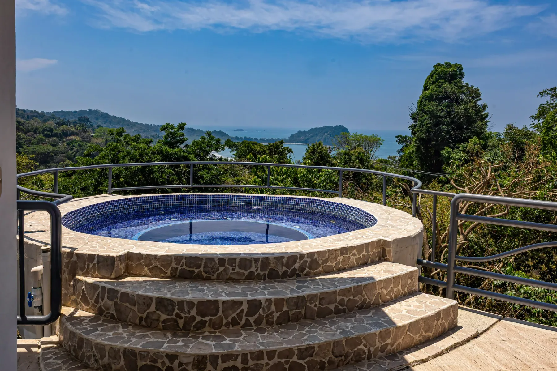 A raised circular spa sits on a stone terrace overlooking a wooded landscape.