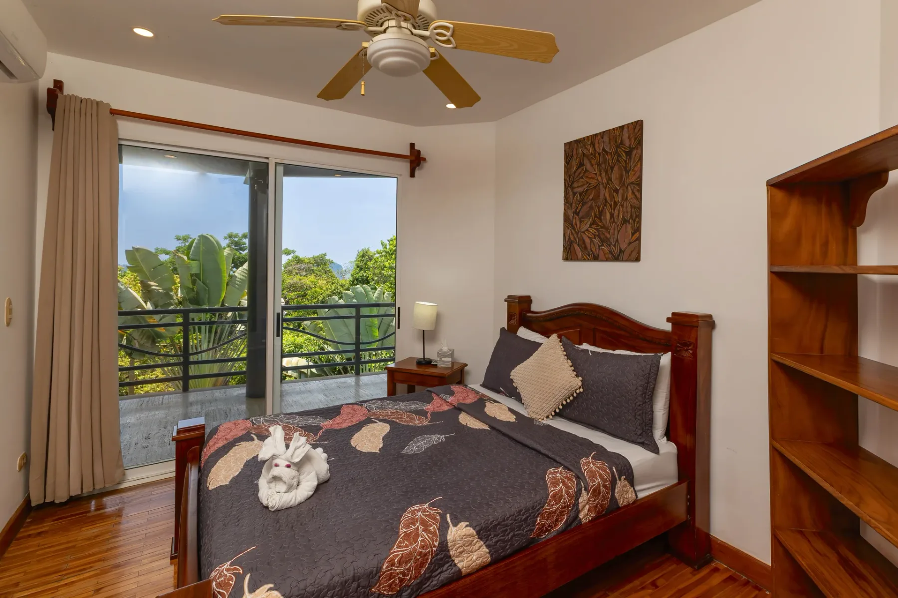 A bedroom with a patterned bedspread and sliding glass doors opening to a balcony.