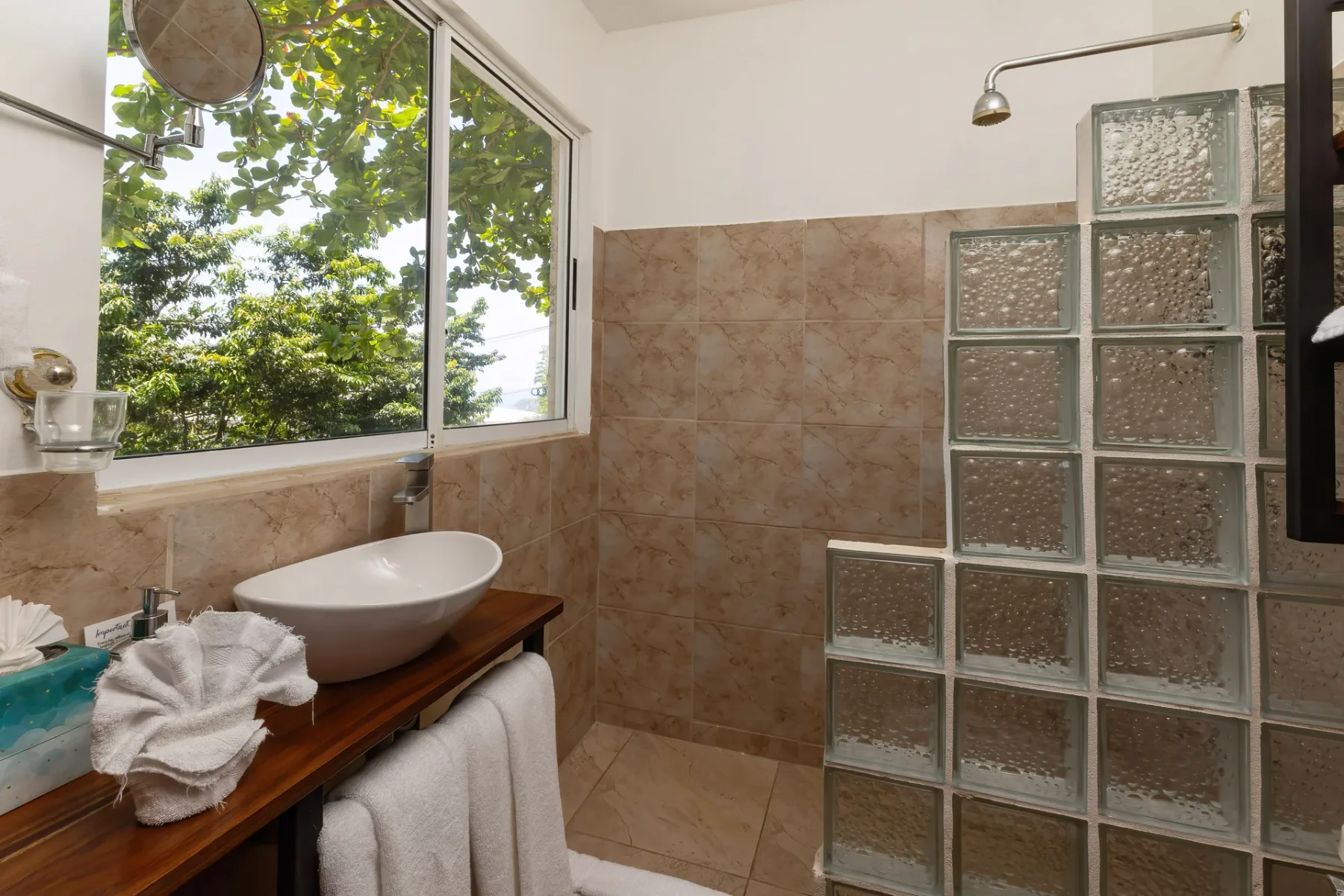 A bathroom with a vessel sink beside a window overlooking leafy greenery.