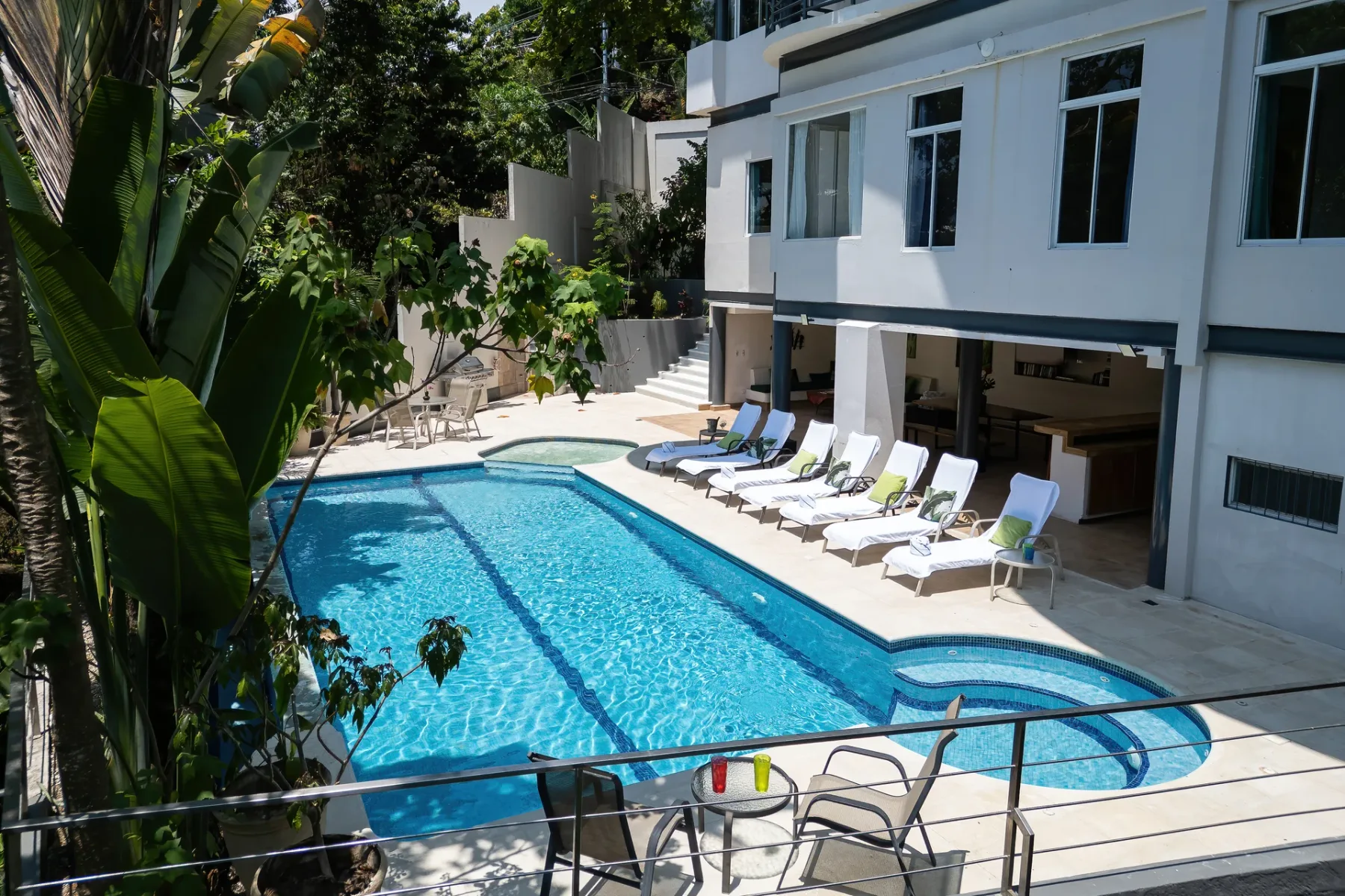 A swimming pool and loungers sit beside a modern white building.