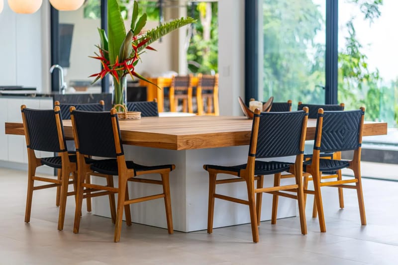 Casa La Vista · 13. This open dining area features a substantial wooden table and woven chairs, flooded with natural light from expansive windows that frame tropical views.