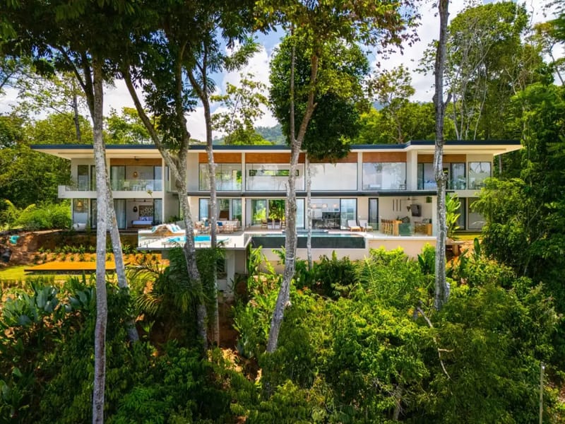 Casa La Vista · 7. A multi-level modern villa is set into a tropical hillside, featuring an infinity pool on a wide terrace, expansive glass walls, and multiple outdoor living areas framed by lush jungle.