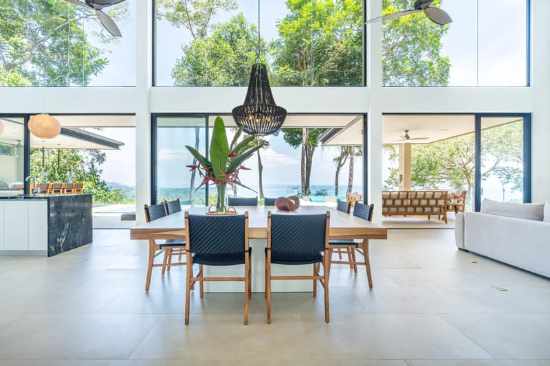 Casa La Vista · 11. This bright, open-concept living space integrates a dining area and features floor-to-ceiling glass walls showcasing panoramic ocean and jungle views.