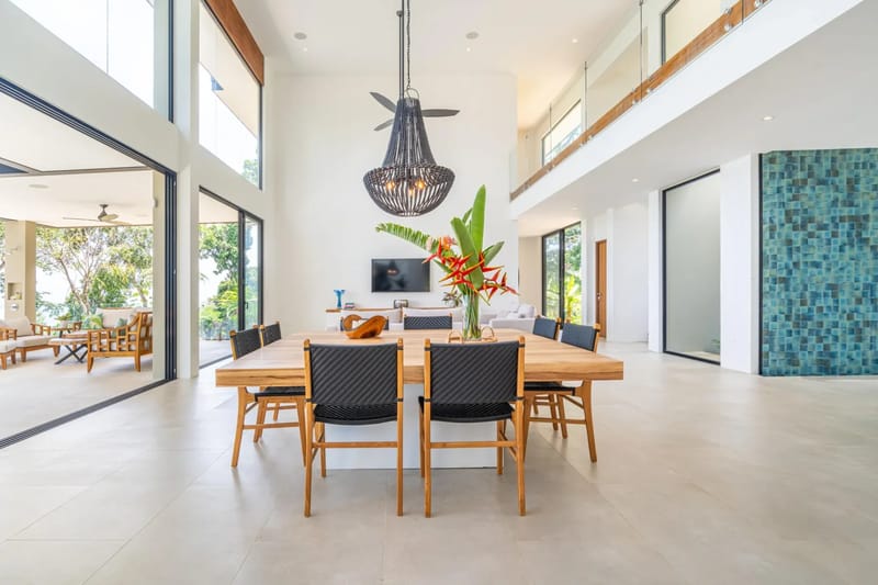 Casa La Vista · 20. A spacious, open-concept dining room with high ceilings and extensive natural light connects directly to an outdoor terrace, offering views of tropical greenery, and is overlooked by a second-story interior balcony.