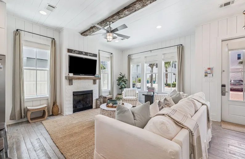 A bright living room with pale seating, a fireplace, and large windows.