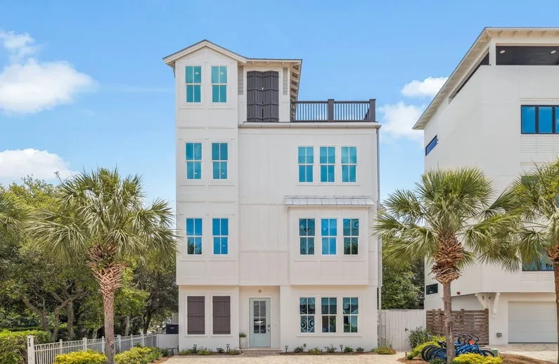 A multi-story white house with blue windows stands among palm trees.