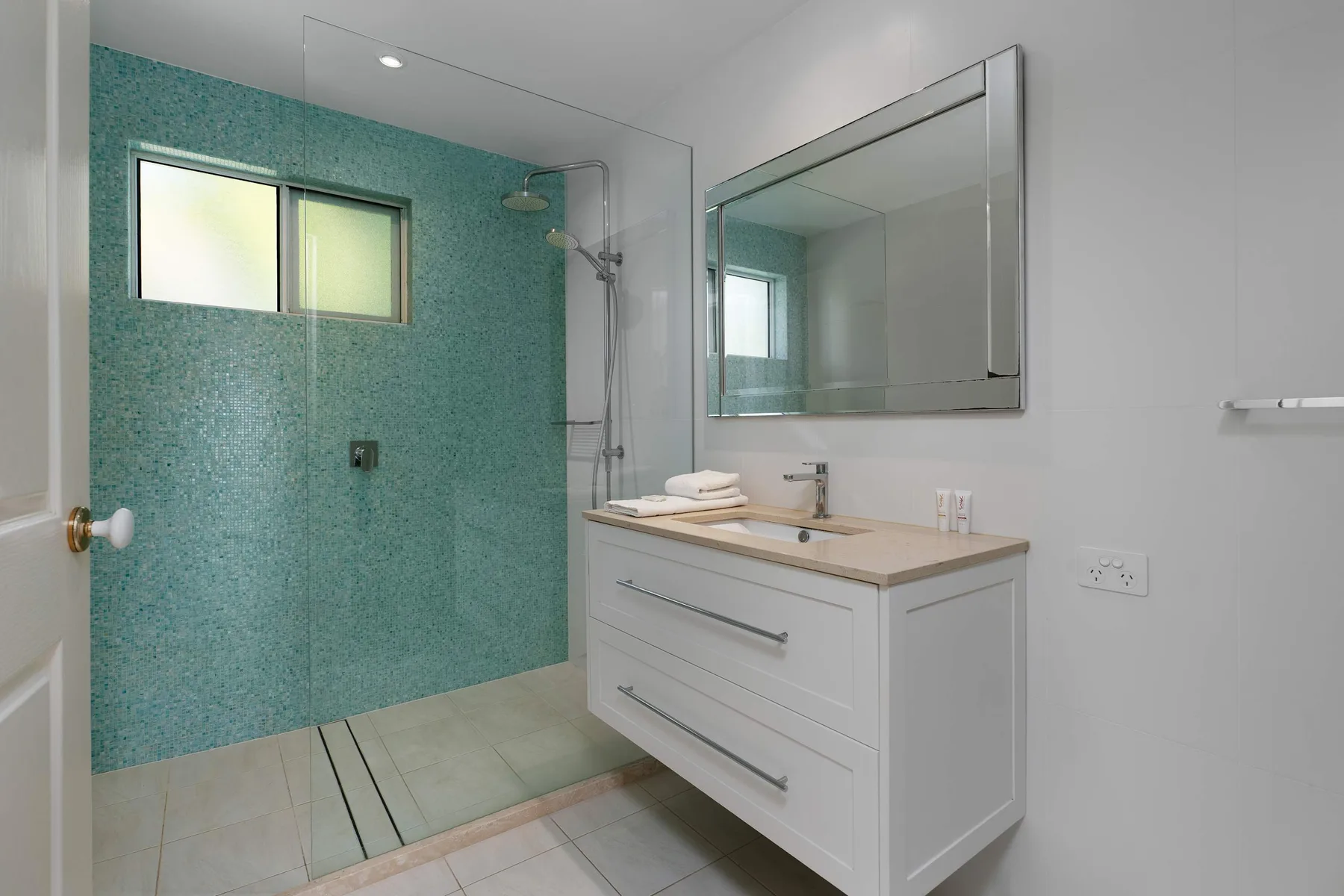 Un baño luminoso con ducha de cristal y un tocador blanco.