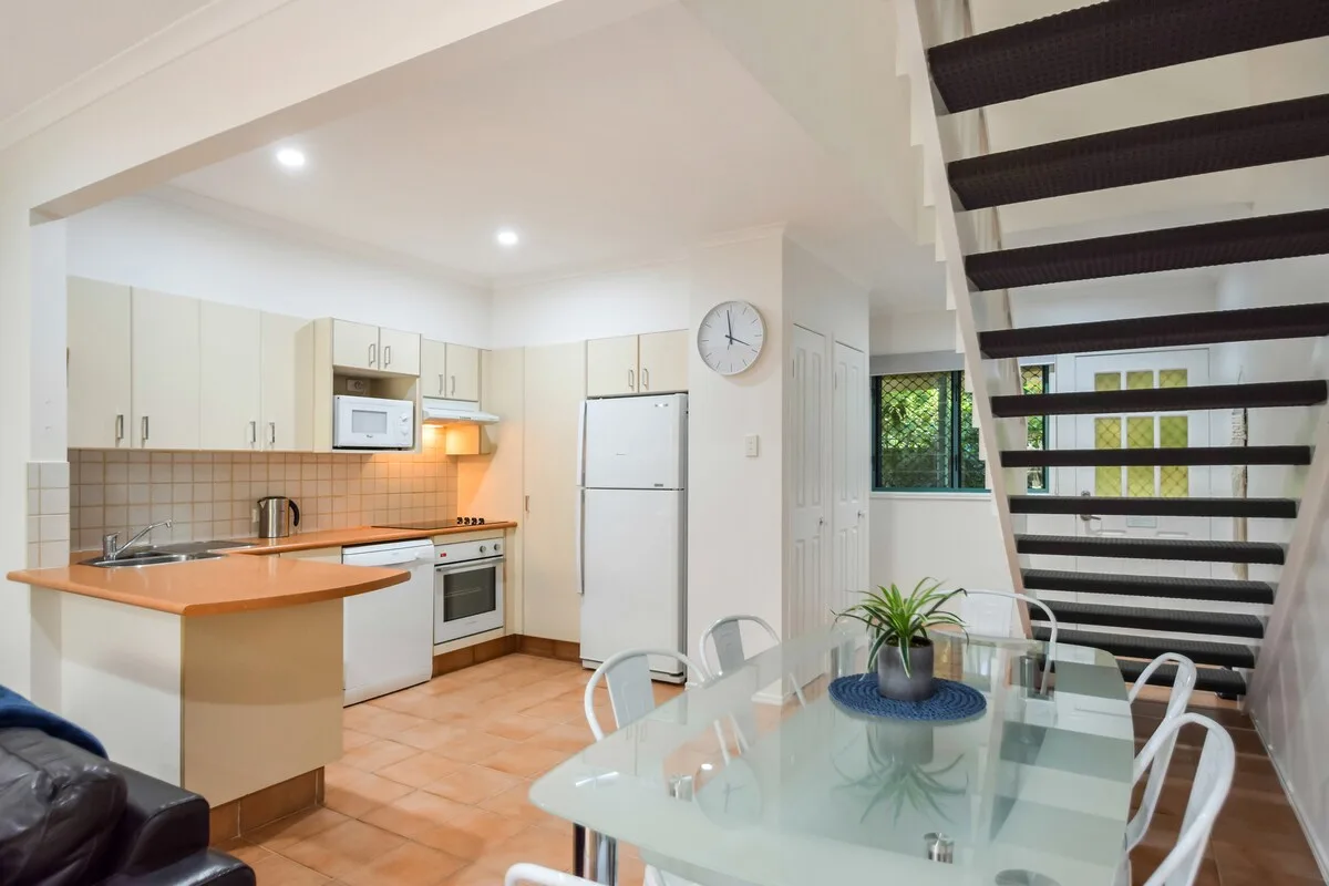 A dining area with a glass table beside an open kitchen and staircase.