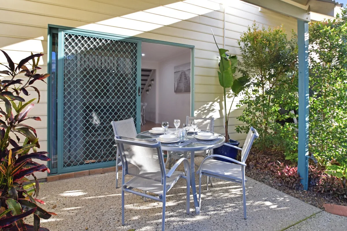 An outdoor patio has a round table set with dishes and metal seating.